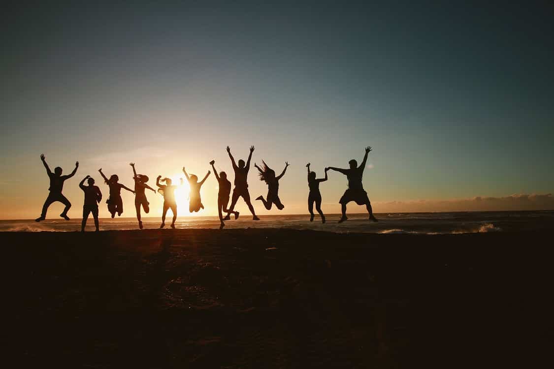 אנשים שמחים קופצים על חוף הים אל מול השמש השוקעת